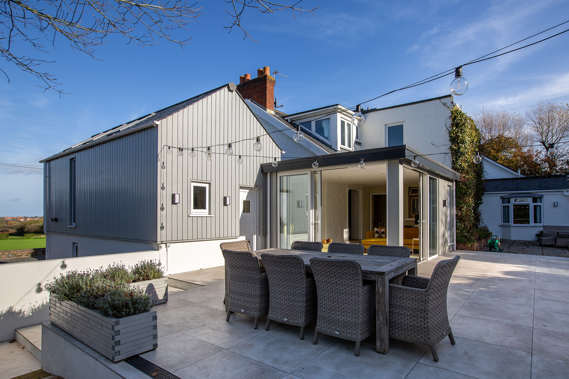 Property with a large patio, festoon lights, table and chairs, and a conservatory