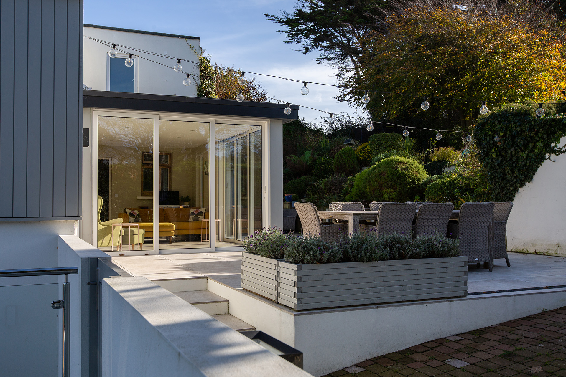 Outdoor photo of a patio with festoon lights, wicker table and chairs, and a conservatory